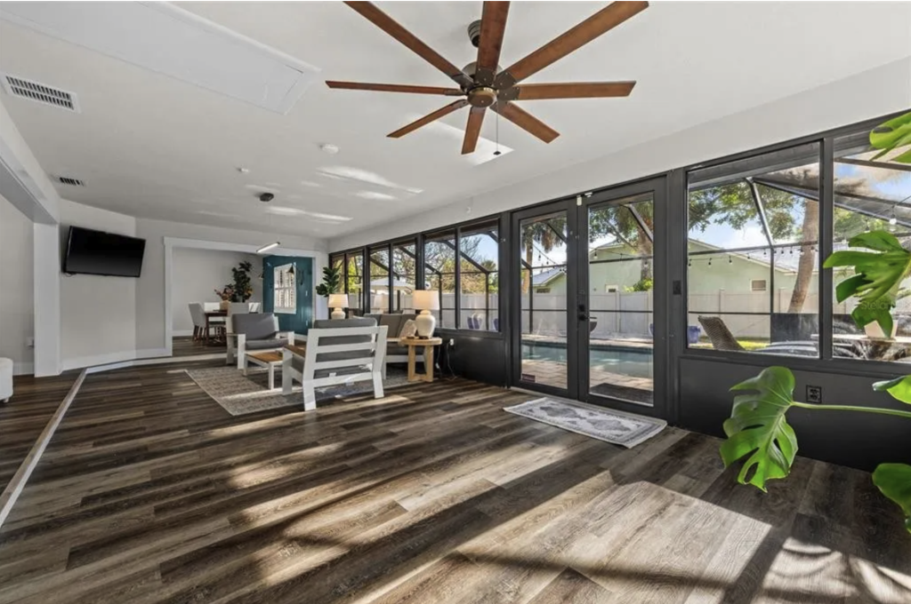 Open-concept Florida living room with a teal accent wall, white furnishings, and large glass doors leading to a screened pool area — an example of how interior painting in Sarasota can define space in open floor plans.