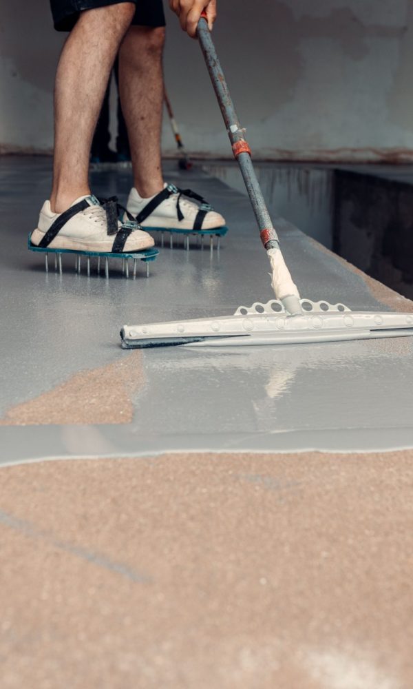 Construction worker applying grey epoxy resin in an industrial hall A construction worker applying grey epoxy resin in an industrial hall